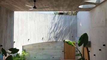 Un espace piscine intérieur moderne avec un plafond en béton, des murs en bois et un ventilateur de plafond.