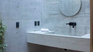 Un baño moderno con pared de concreto, un espejo redondo, un lavamanos blanco y una planta en maceta.