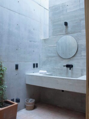 A modern bathroom with a concrete wall, a round mirror, a white sink, and a potted plant. - 2BR Architectural Retreat with Private Pool NEW (Brisas de Zicatela)