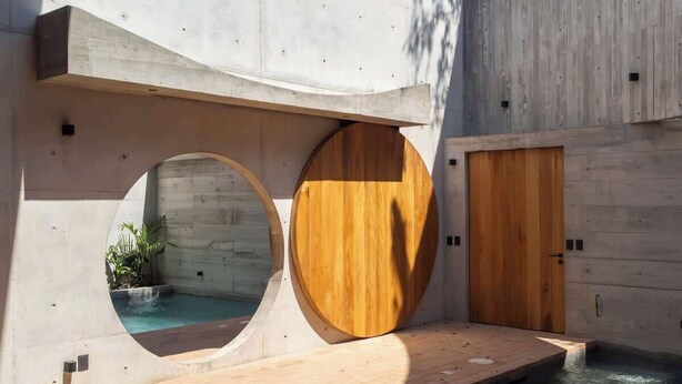 Diseño arquitectónico moderno con puertas de madera circulares, una piscina y una estructura de concreto.