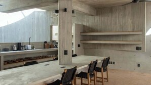 Una cocina moderna con encimera de concreto, sillas de madera y estanterías empotradas.