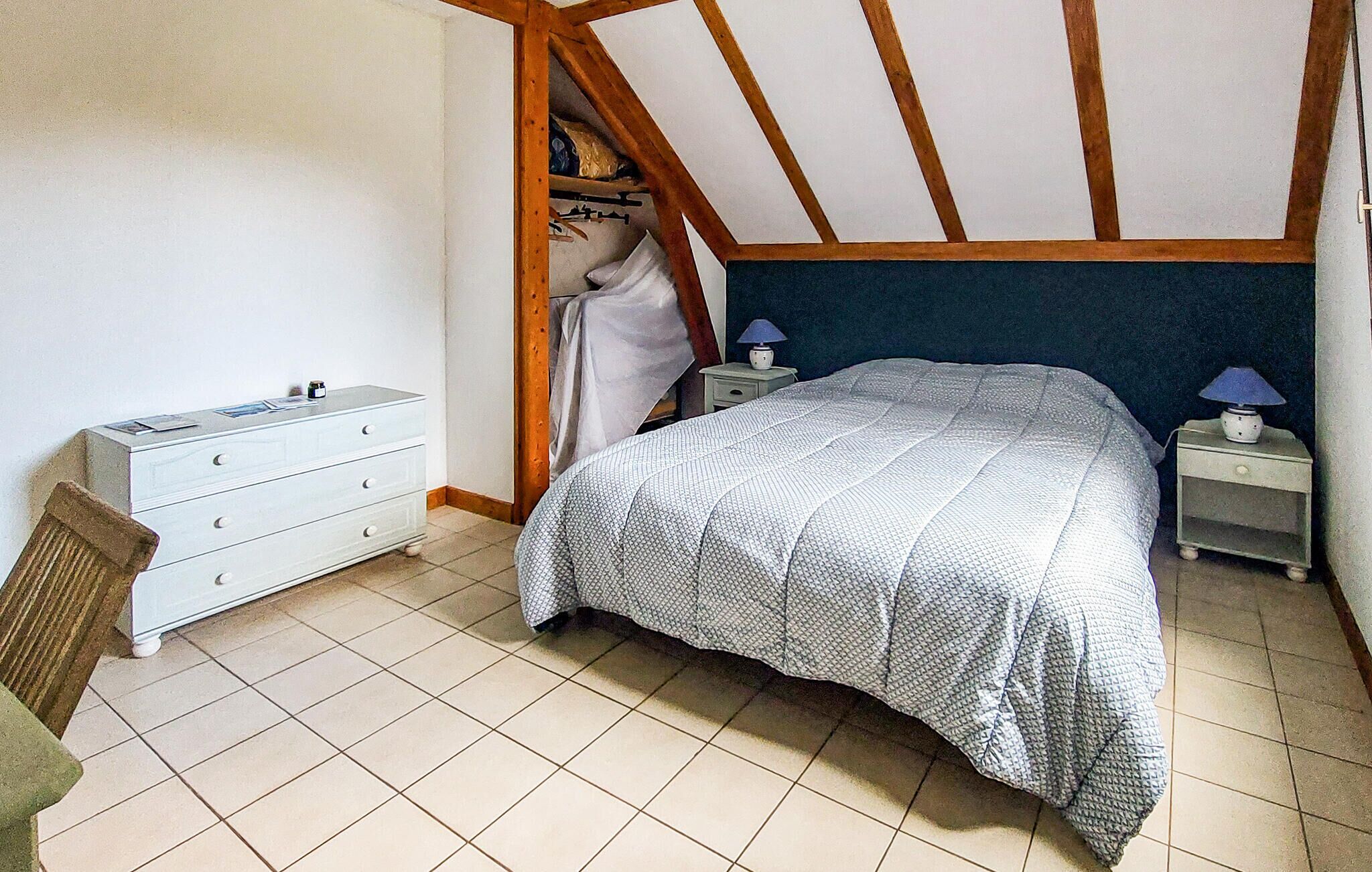 A bedroom with a bed, a dresser, a chair, and a nightstand with a lamp.