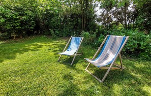 Zwei gestreifte Liegestühle in einem grünen Gartenbereich, im Hintergrund dichtes Laub.