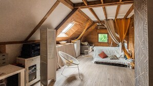 Un dormitorio acogedor en el ático, con techo inclinado, una cama, una mesita y una silla.