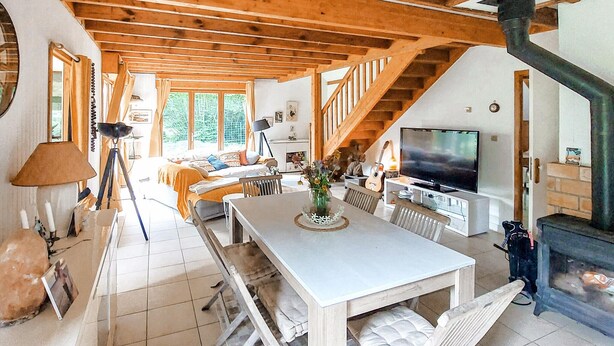 Un amplio salón con techo alto, vigas de madera, una mesa de comedor, una chimenea y un televisor.