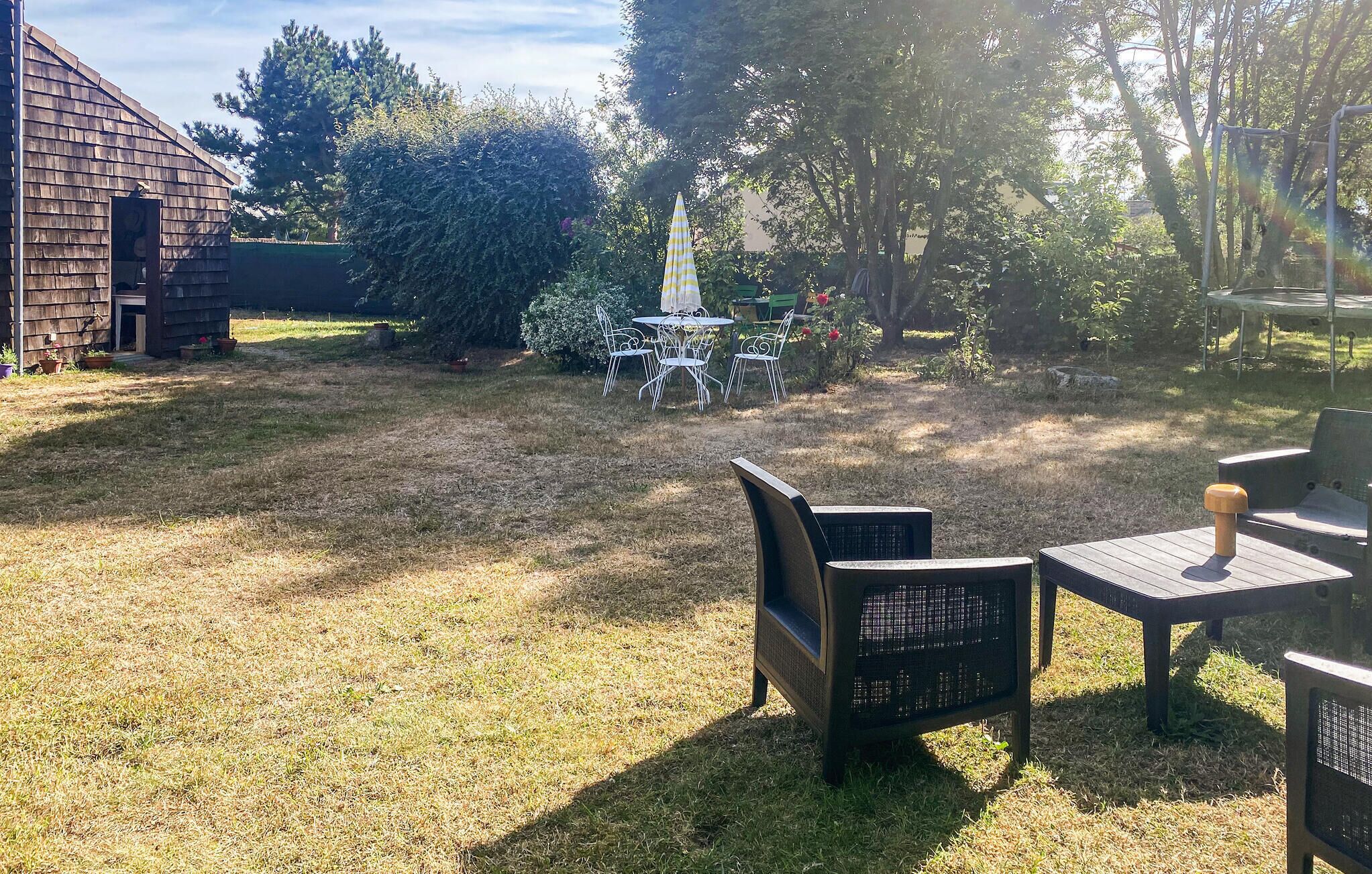 Ein Garten mit einer Holzterrasse, einem Tisch mit Stühlen und einem kleinen Gartenbereich mit Hecke und Baum.