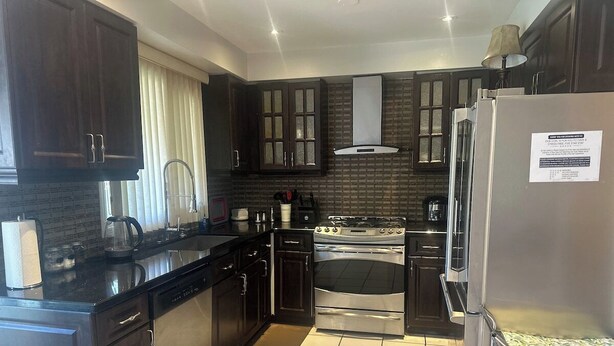 A modern kitchen with dark cabinetry, a stainless steel refrigerator, a gas stove, and a built-in oven. - Private Room Near SQ 1 • Self Check-in • 2 min to Transit (Mississauga)