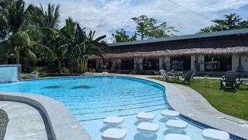 A swimming pool with lounge chairs and a thatched-roof building.