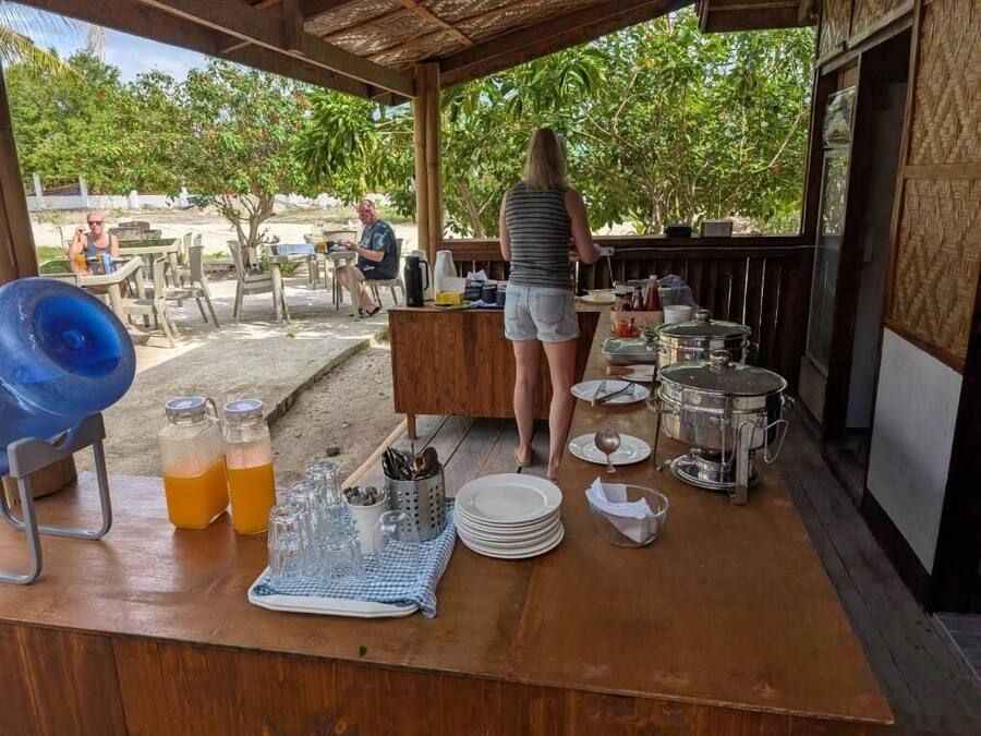 Un espacio cubierto para comer al aire libre, con una mesa de madera, sillas y una mesa de buffet.