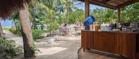 An outdoor bar area with a wooden counter, seating, and a view of palm trees and the ocean.