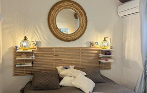 Ein Schlafzimmer mit einem Holzlamellen-Kopfteil, einem runden Spiegel, Nachttischlampen und einem Bett mit Kissen.