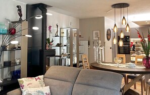 Ein modernes Wohnzimmer mit einem grauen Sofa, einem Esstisch mit Stühlen, einem schwarzen Bücherregal und Dekorationselementen.