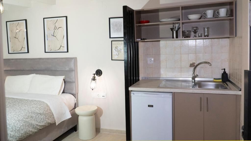 Una habitación pequeña con cama, lavamanos y refrigerador compacto.