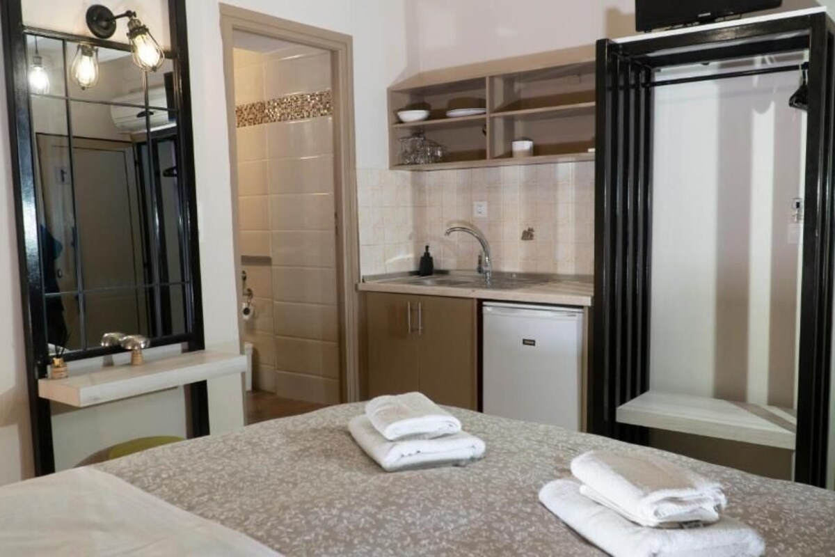 Una habitación de hotel con cama, un baño con lavamanos y espejo, y una kitchenette con refrigerador.