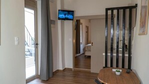 Ein Flur mit einem an der Wand befestigten Fernseher, einer Tür zu einer Treppe und einem runden Tisch mit einer Fernbedienung.