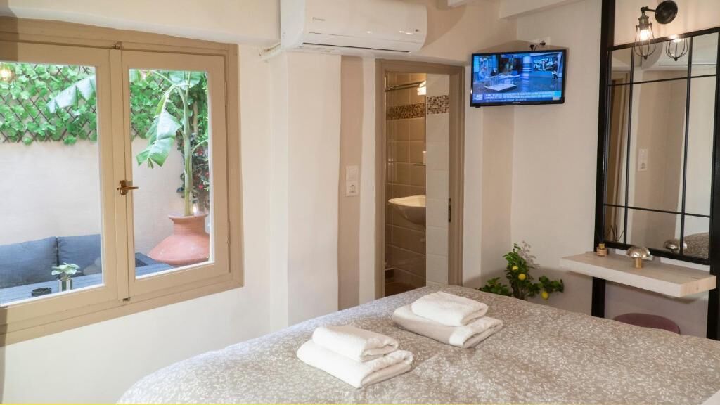 A hotel room with a bed, a TV, a bathroom, and a view of greenery outside.