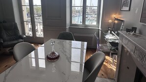 Ein Essbereich mit einem Marmortisch, Stühlen, einer Fernbedienung und Blick auf eine Marina durch große Fenster.