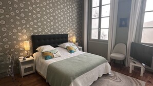 Ein Schlafzimmer mit einem Bett, Nachttischlampen, einem Fernseher, einem Sessel und einer Wand mit Muster.