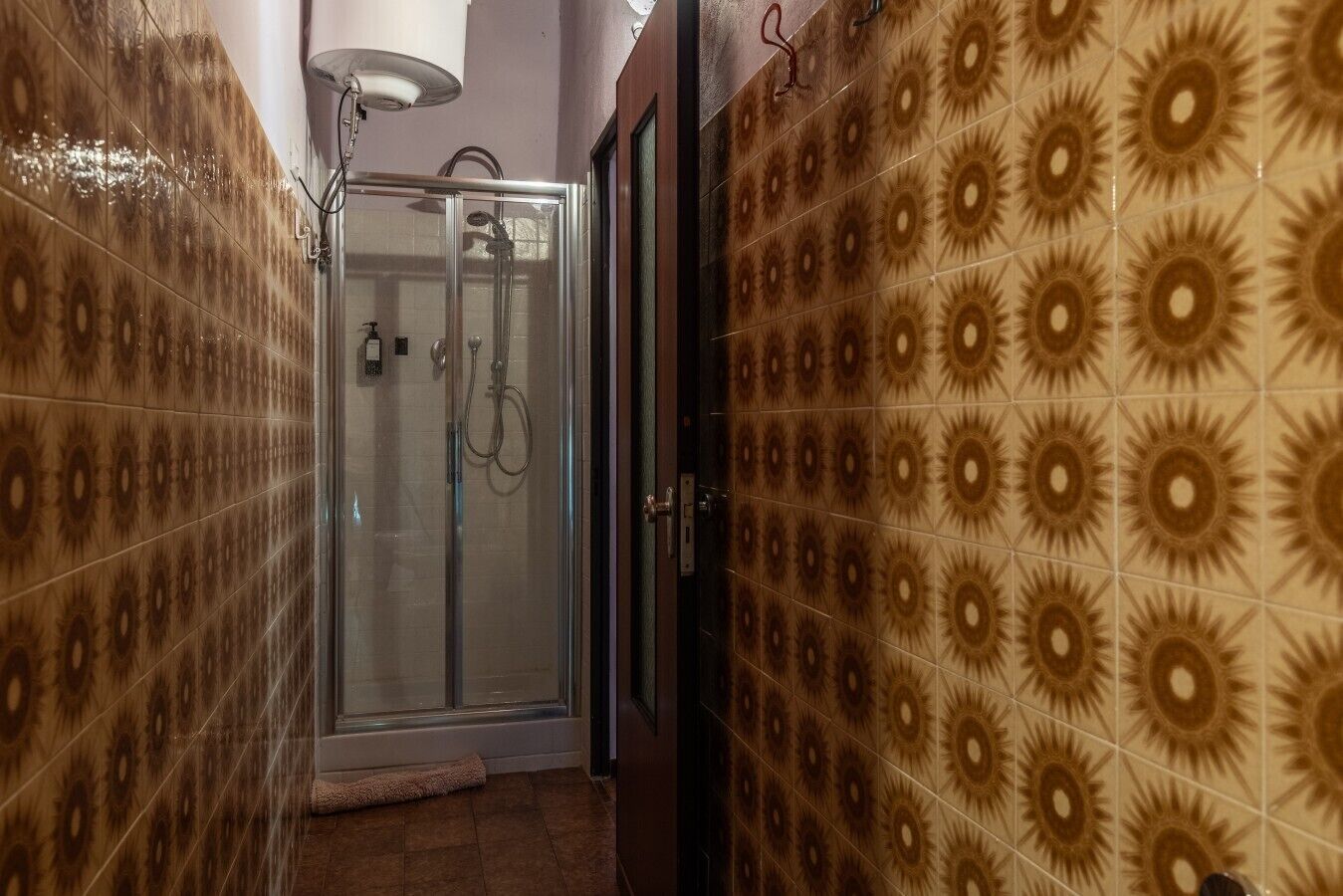 Ein Badezimmer mit gemusterten Fliesen, einer Glasdusche und einem Handtuch auf dem Boden.