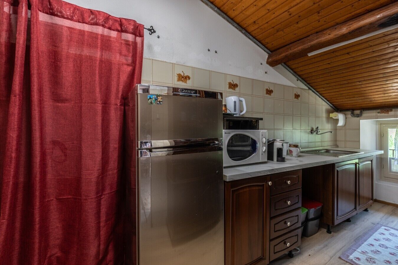 Eine Küche mit Kühlschrank, Mikrowelle und Kaffeemaschine, Holzschränken und einem Fenster mit Blick.