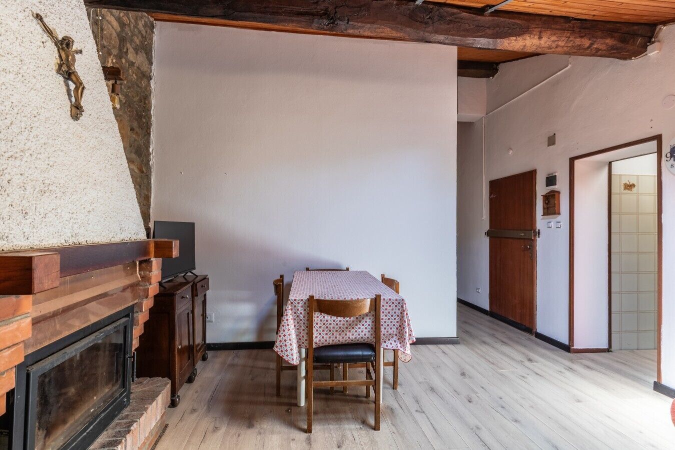 A room with a fireplace, a table with a tablecloth, wooden flooring, and a door with a number.