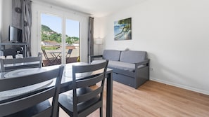 Ein Zimmer mit Esstisch, Stühlen, einer Couch, einem Gemälde und Blick auf einen Hügel.