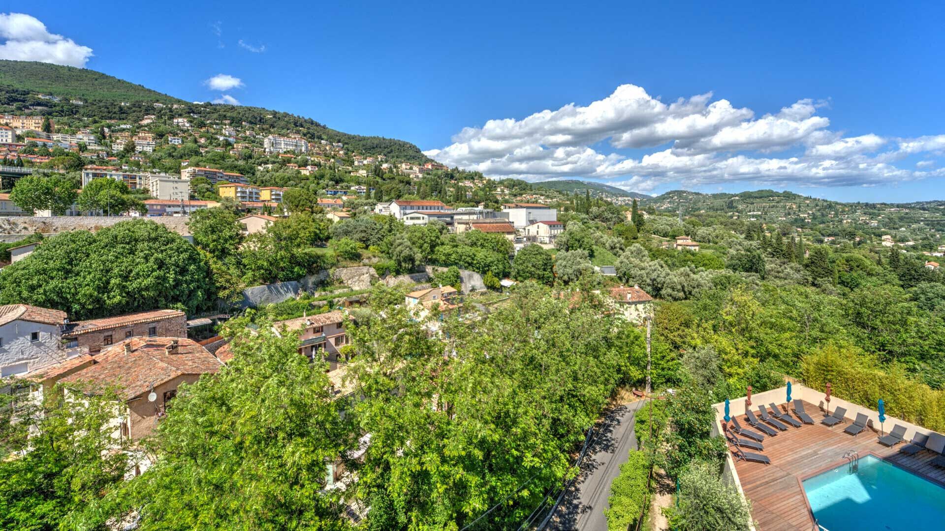Una villa en la ladera con piscina, rodeada de vegetación exuberante y vistas al pueblo.