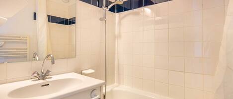 A bathroom with a white sink, a mirror, a shower with a handheld showerhead, and a bathtub.