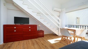 A modern room with a staircase, a TV on a wooden cabinet, a dining table with chairs, and a balcony with a view. - Cute studio apartment for 4 people, with a loft and balcony (Agde)