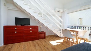 Ein modernes Zimmer mit einer Treppe, einem Fernseher auf einem Holzschrank, einem Esstisch mit Stühlen und einem Balkon mit Aussicht.