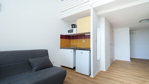 A compact living space with a kitchenette, a grey sofa, and a wooden floor. - Cute studio apartment for 4 people, with a loft and balcony (Agde)
