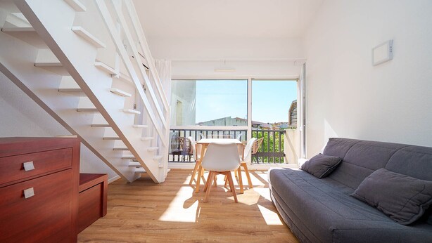 A modern apartment with a staircase, a balcony with a table and chairs, and a grey sofa. - Cute studio apartment for 4 people, with a loft and balcony (Agde)