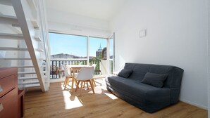 A balcony with a table and chairs, a grey sofa, and a wooden floor. - Cute studio apartment for 4 people, with a loft and balcony (Agde)