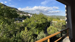Un balcon offrant une vue sur une ville perchée sur une colline, des arbres et un ciel dégagé.