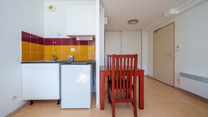 Uma cozinha compacta com geladeira, pia e uma mesa de jantar de madeira com cadeiras.