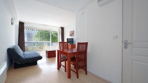 Quarto com cama, mesa de jantar com cadeiras, televisão e janela com cortinas.