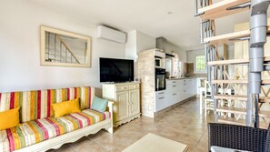 A living room with a sofa, TV, and kitchen area with cabinets and a microwave. - Beautiful Villa - Sleeps 6 - Family-friendly (Homps)