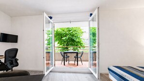 A room with a bed, a desk, a chair, and a table with chairs. There is a TV mounted on the wall and a sliding glass door leading to an outdoor area with a table and chairs. - Charming Studio - Sleeps 2 - Bright (Grasse)