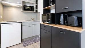 A compact kitchen with a microwave, coffee maker, and toaster on shelves, a small refrigerator, and a patterned rug. - Charming Studio - Sleeps 2 - Bright (Grasse)