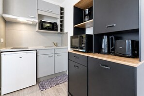 Eine kompakte Küche mit Mikrowelle, Kaffeemaschine und Toaster auf Regalen, einer kleinen Kühlbox und einem gemusterten Teppich.
