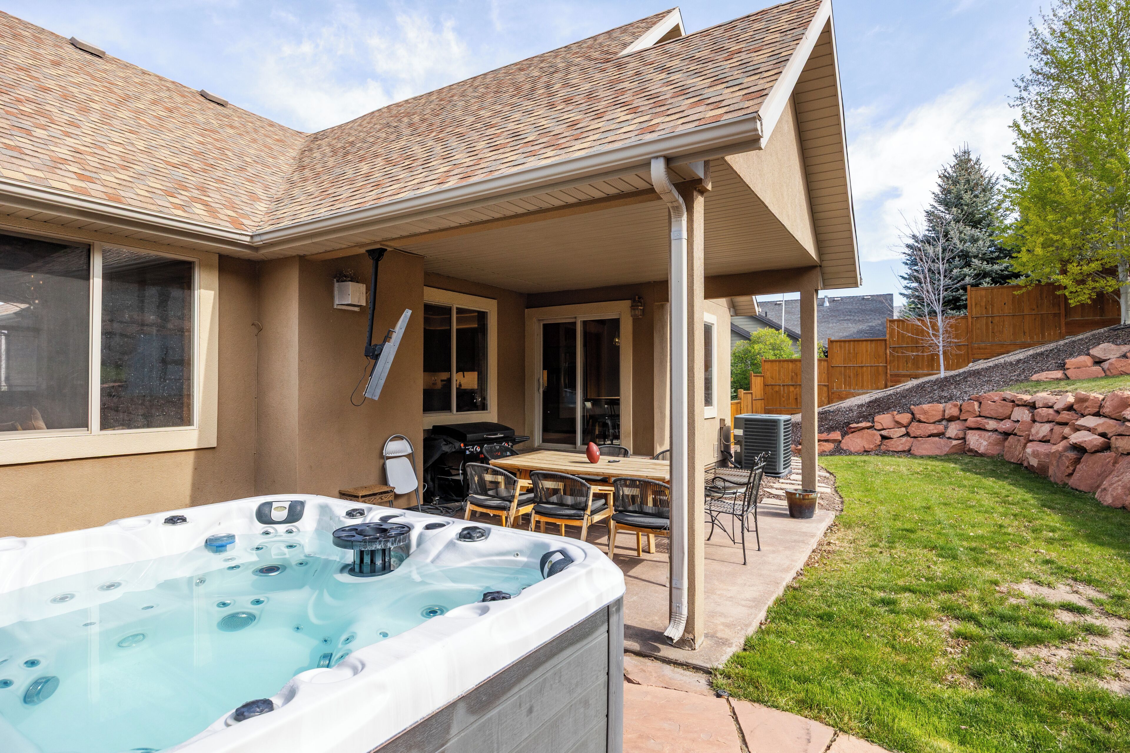 A residential backyard with a hot tub, patio furniture, and a stone retaining wall.