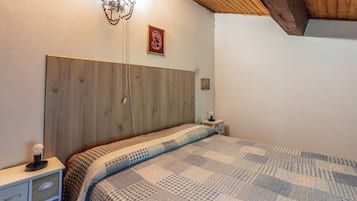 A bedroom with a wooden headboard, a patterned bedspread, a bedside table with a lamp, and a wall-mounted light fixture.