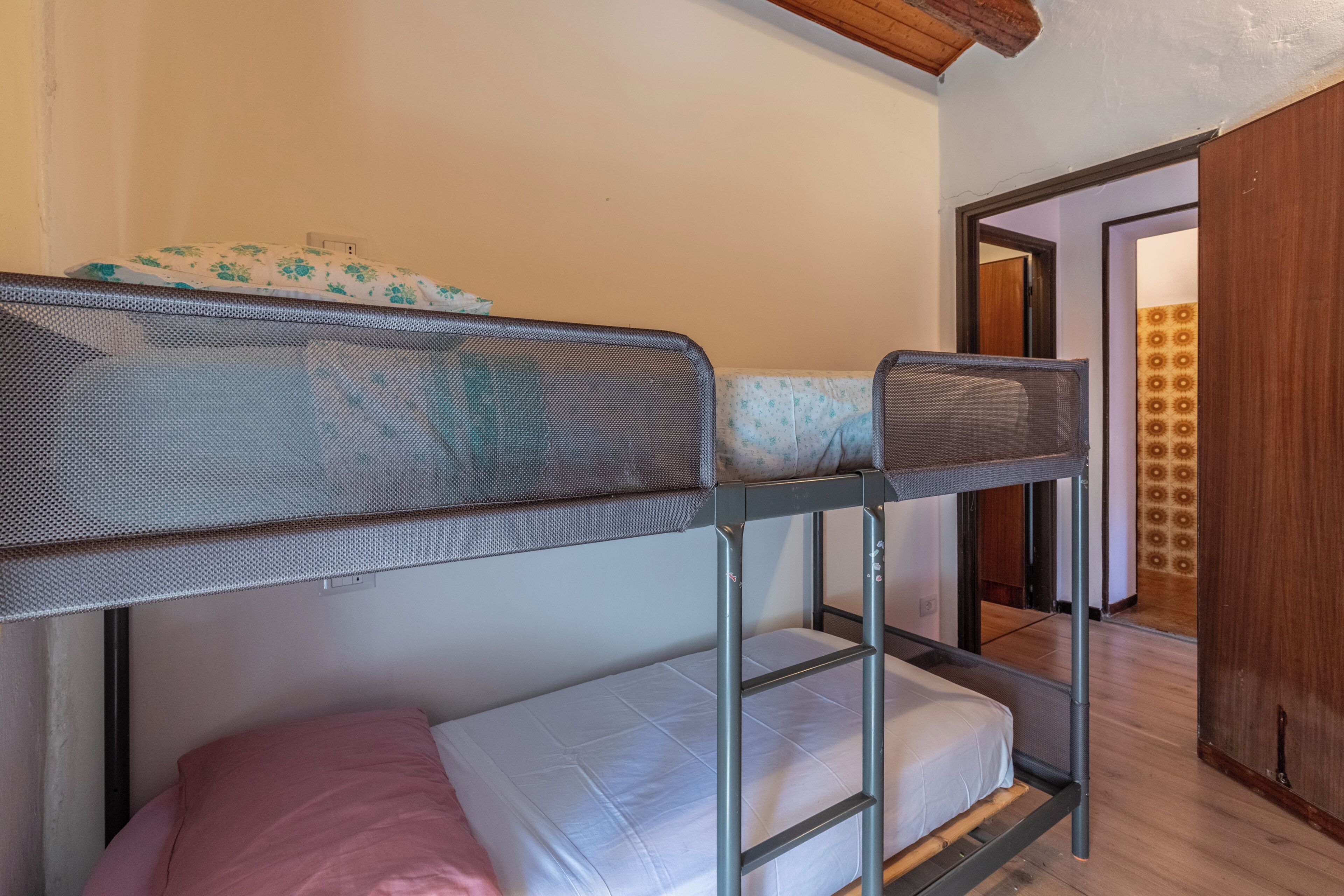 Un letto a castello con una testiera a rete e un giroletto inferiore con un cuscino rosa.