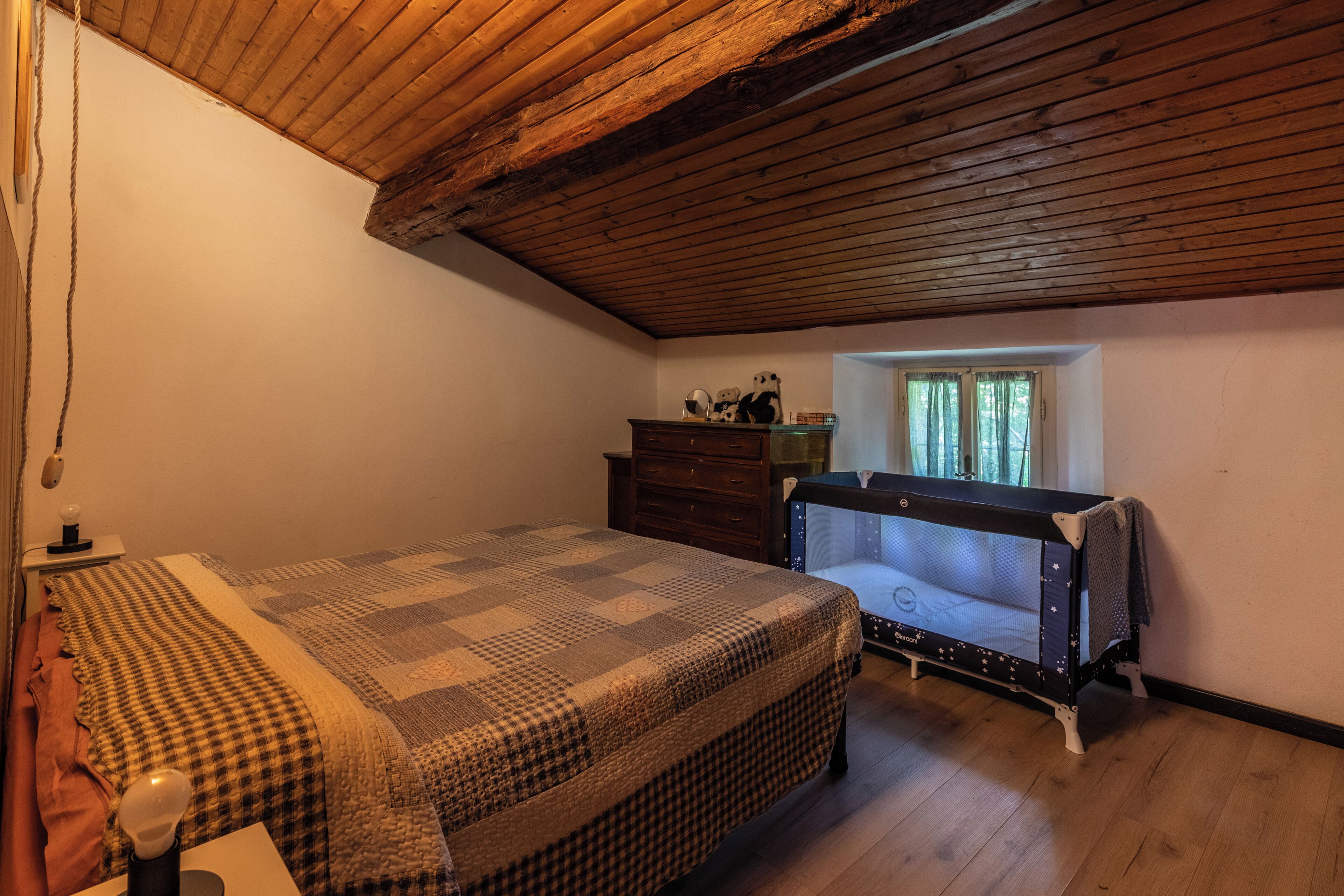 Une chambre à coucher avec un lit, un berceau, une commode et une fenêtre avec des rideaux.