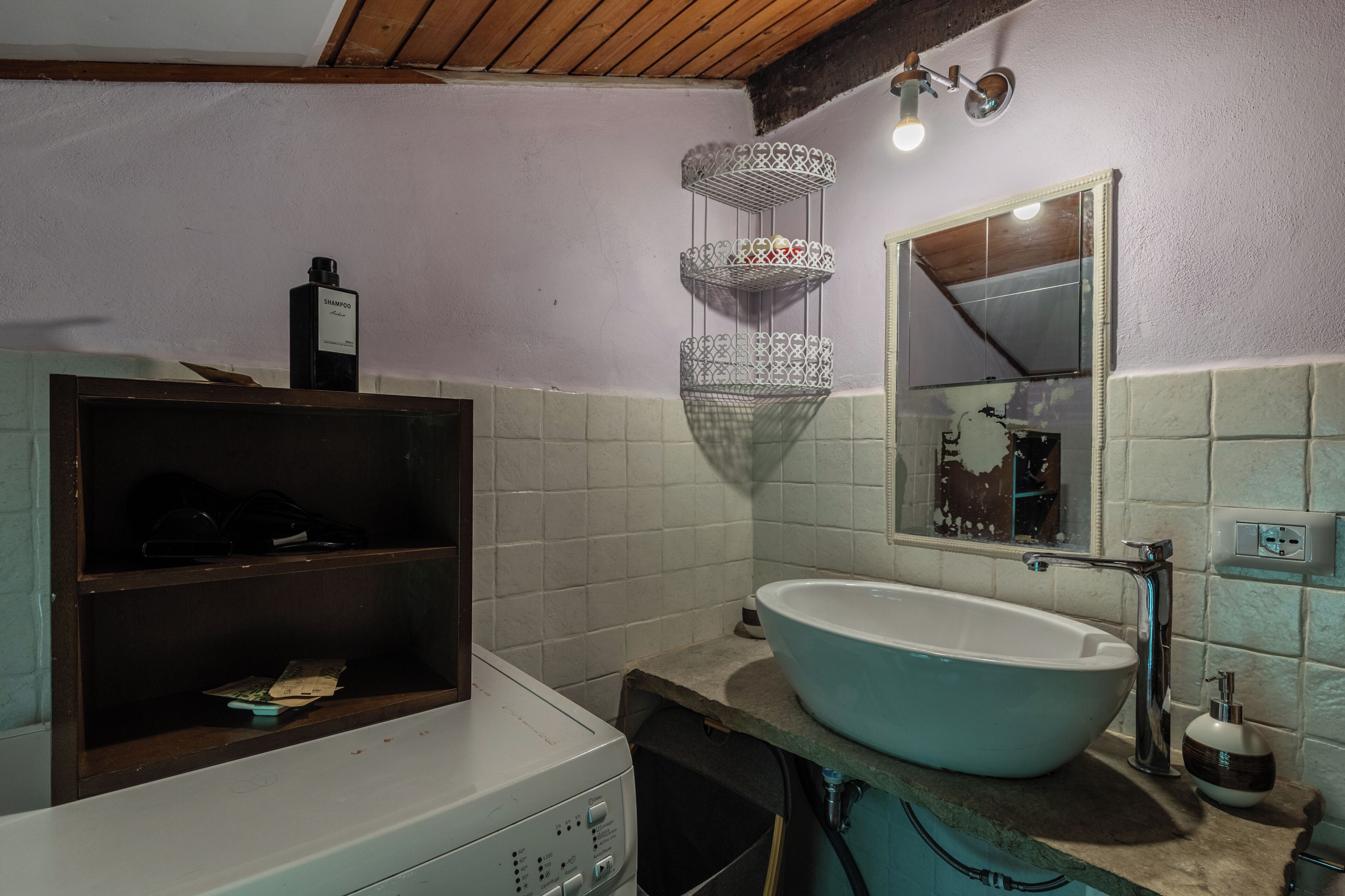 Un bagno con un lavandino bianco, uno specchio, uno scaffale con articoli da toilette e un lampadario.