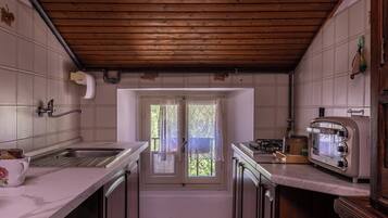Eine Küche mit Holzbalkendecke, einem Fenster mit Spitzenvorhängen, einer Spüle, einem Herd und einem alten Toaster.