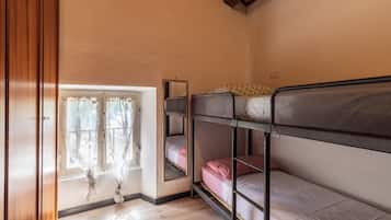A dormitory room with bunk beds, a window with curtains, and a wooden floor.