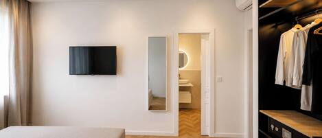 A modern hotel room with a bed, a TV, a mirror, a wardrobe, and a bathroom visible through an open door.