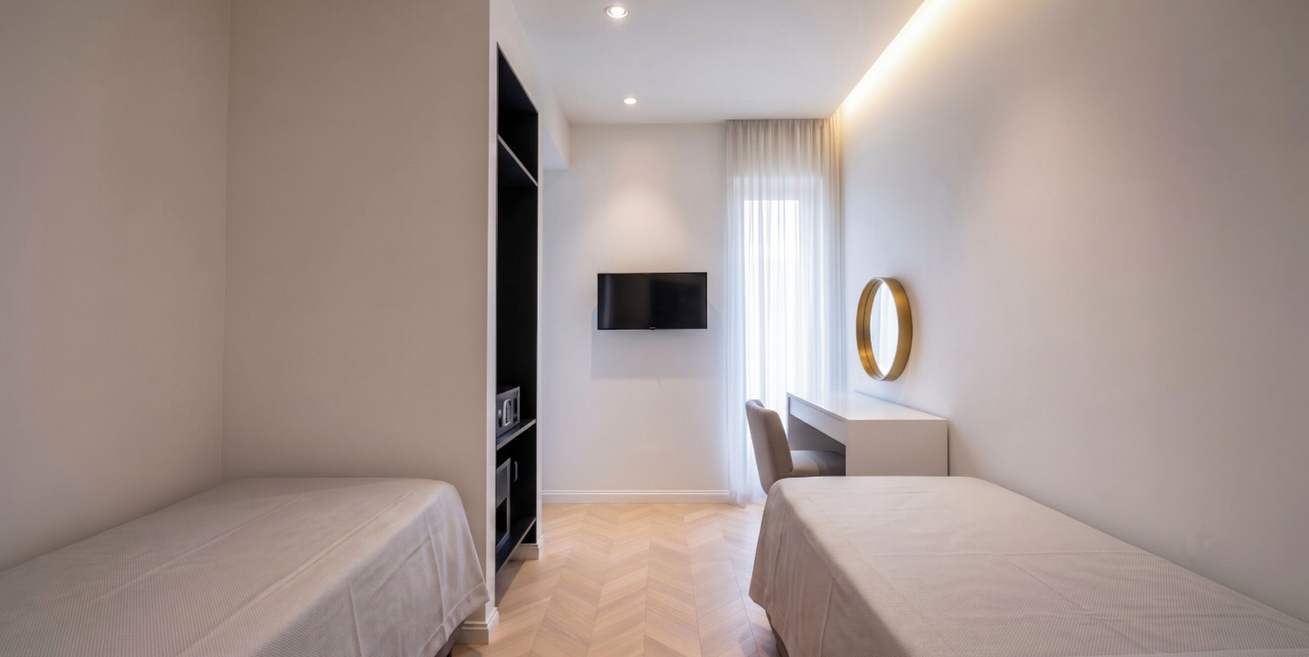 A hotel room with two beds, a desk, a TV, and a wardrobe.