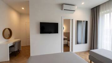 A modern hotel room with a bed, a TV, a desk, and a door leading to a bathroom.